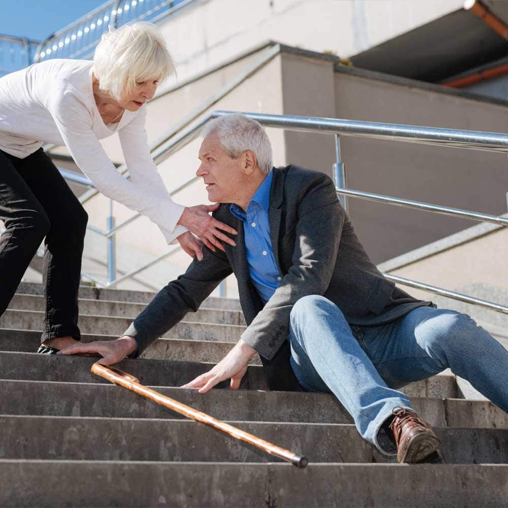 Un homme senior chute dans les escaliers, sa femme tente de l'aider