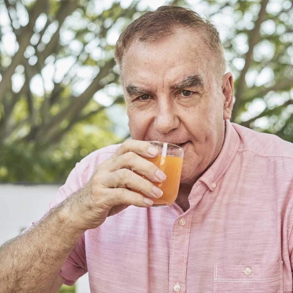 Un homme senior boit un jus d'orange pour prévenir une anémie